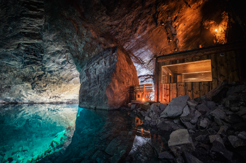 A cave with a small wooden building and a pool of water

AI-generated content may be incorrect.