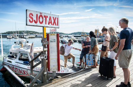 A group of people on a dock with a sign and boats

